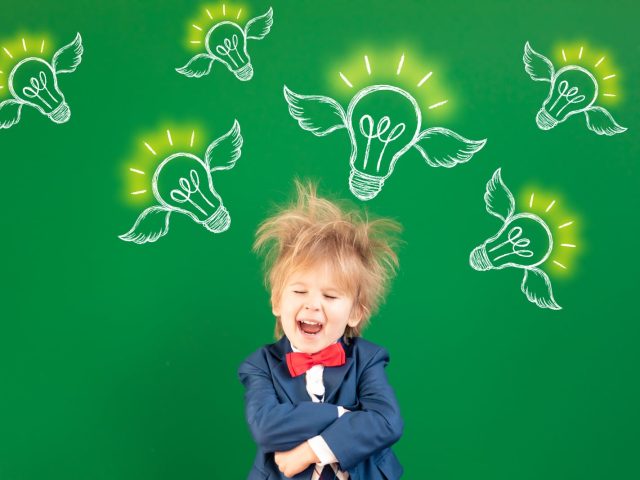 Be strong! Happy child in class. Smiling kid against green chalkboard. Portrait of student indoor. Imagination and dream concept. Back to school